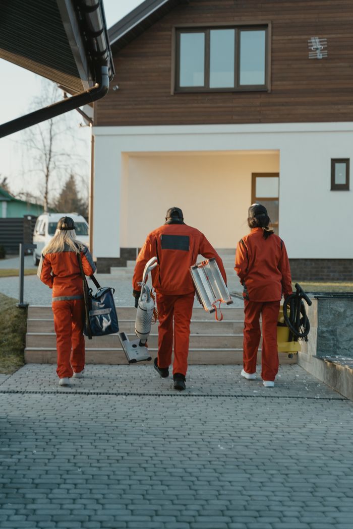 creative-03 Une équipe de nettoyage en uniformes rouges, équipée et en approche de la façade d’une maison moderne.